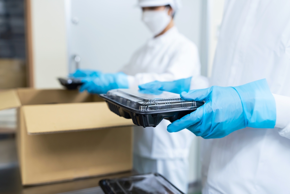 two men in sterile uniforms placing thermoformed food trays in a cardboard box